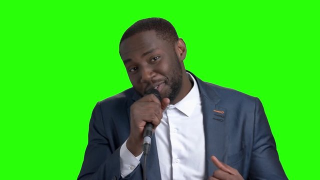 Smiling man with microphone on green screen. The afro-american entertainer holding miocrophone on Alpha Channel background.