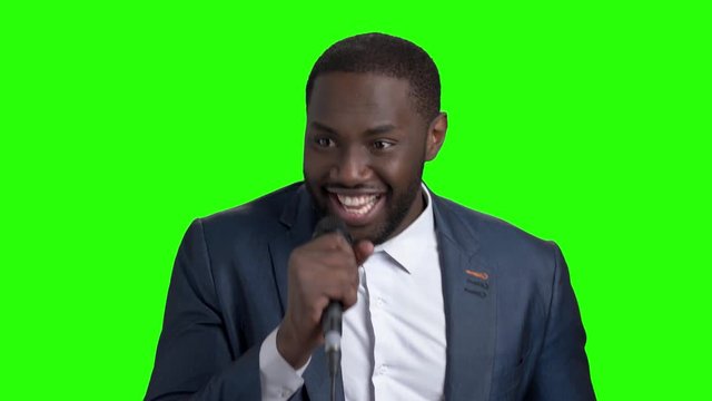 Young elegant man talking into microphone. Handsome afro-american entertainer is singing on chroma key background. People, entertainment, media.