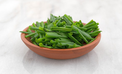 Bowl of cut chives atop a gray marble cutting board.