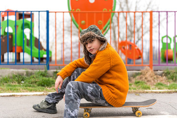 Young urban boy sitting on his skateboard on the street, waiting his friends, looking to camera
