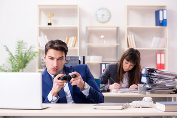 Man playing games in office while colleague is busy