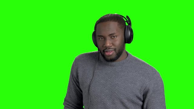 Afro american guy is dancing on green screen. Portrait of handsome dark-skinned man with headphones dancing on chroma key background.