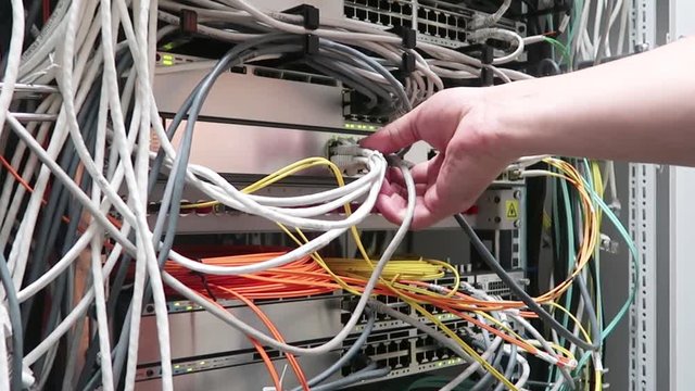 One male IT engineer working in a data center with rows of server racks and super computers. He is checking all of the cables and other equipment. Сhecking the network cable RG45.