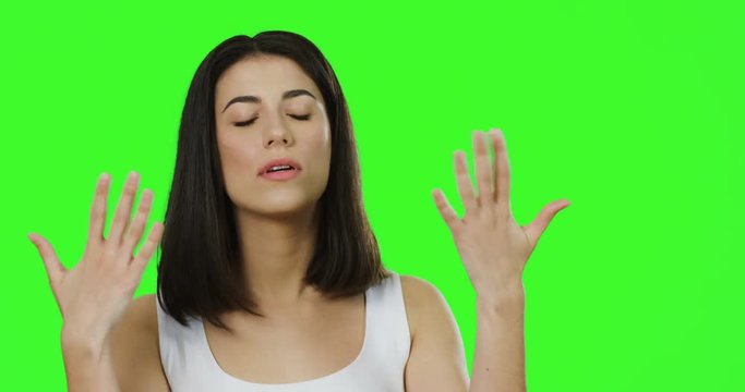 Close up of the young brunette woman in the white shirt waving hands as it is hot on the chroma key background. Green screen