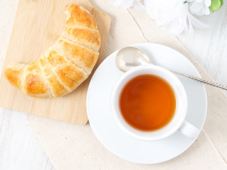 Cup of tea, flowers and fresh baked puff pastry on a white table. Delicious croissants, top view, close up