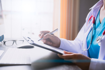 Soft focus of Female doctor hand holding application form or check list at office table with computer. Healthcare And Medical concept.