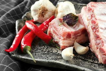 Plate with fresh raw pork ribs, garlic and chili on black napkin