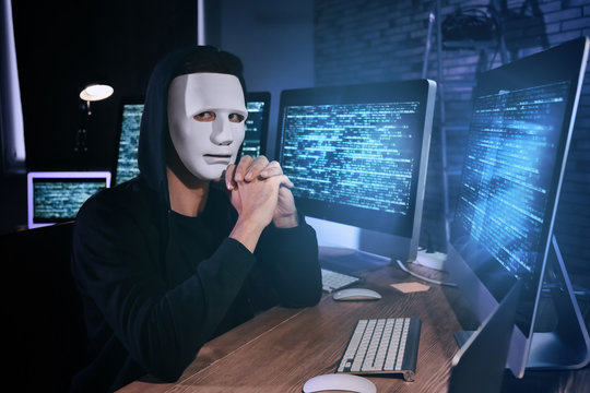 Masked hacker in dark room with computers. Threat of cyber attack