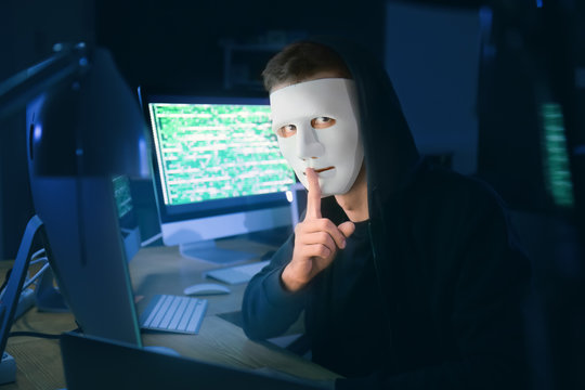 Masked hacker in dark room with computers. Threat of cyber attack