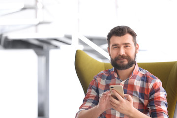 Portrait of confident mature man with mobile phone in armchair