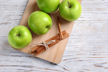 Fresh apples and cinnamon sticks on wooden board, top view