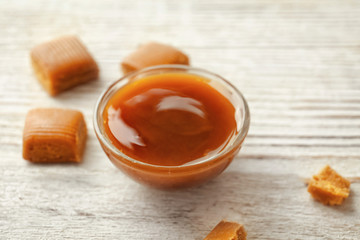 Delicious caramel candies and sauce on wooden background