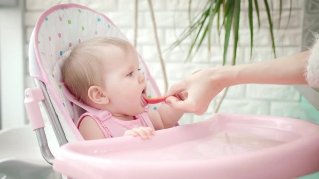 Sweet baby girl eating vegetable. Close up of mother hand feeding child with red pepper. Baby healthy food. Toddler in chair tasting new meal. Little kid eat vegetables. Child have dinner