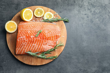 Wooden board with raw salmon and ingredients for marinade on grey background, top view