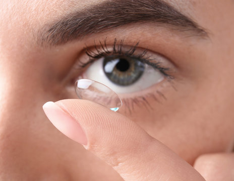 Young woman putting contact lens in her eye, closeup