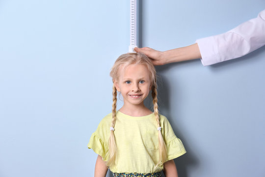 Doctor measuring little girl's height on light background