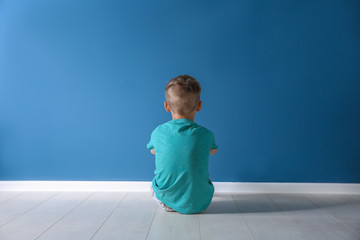 Little boy sitting on floor near color wall in empty room. Autism concept