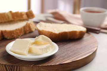 Plate with tasty butter and fresh bread on wooden board