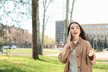 Young woman talking by phone outdoors on sunny day