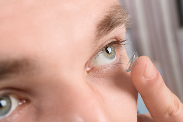Naklejka premium Young man putting contact lens into his eye, closeup