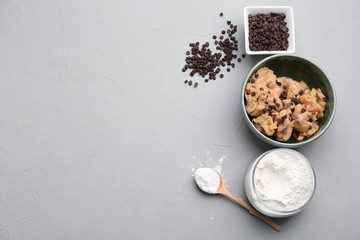 Flat lay composition with cookie dough, chocolate chips and flour on grey background