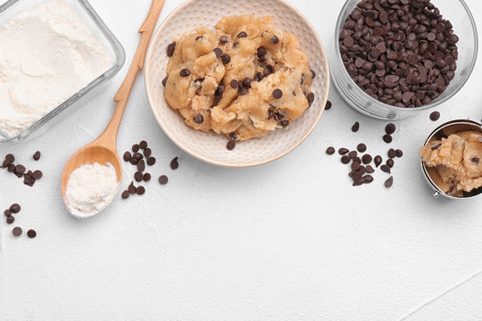Flat lay composition with cookie dough, chocolate chips and flour on light background