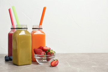 Bottles with healthy detox smoothies and bowl of strawberries on table