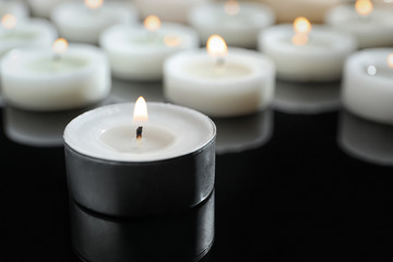 Wax candles burning on table in darkness, closeup