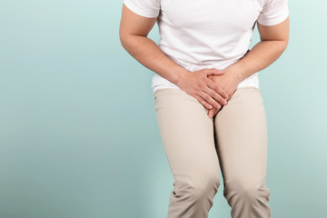 Young man with urological problems suffering from pain on color background