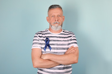 Mature man with blue ribbon on color background. Urological cancer awareness