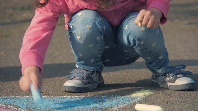 The child is drawing. The girl draws chalk on the asphalt.