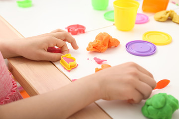 Obraz na płótnie Canvas Cute little girl using play dough at table, closeup