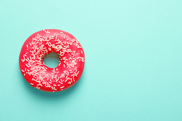 Delicious glazed doughnut with sprinkles on color background, top view