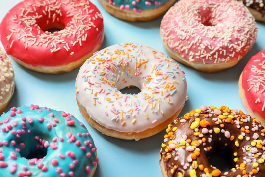 Delicious glazed doughnuts with sprinkles on color background