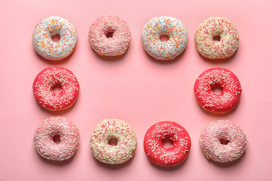 Frame made of delicious glazed doughnuts on color background, top view