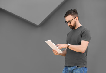 Portrait of young man with tablet near grey wall