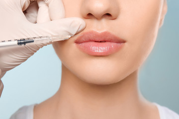 Young woman getting lip injection on color background, closeup