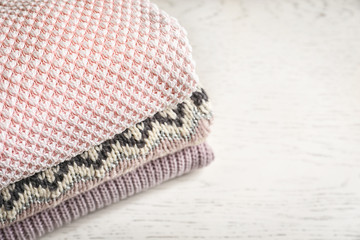 Stack of warm knitted clothes on light background, closeup