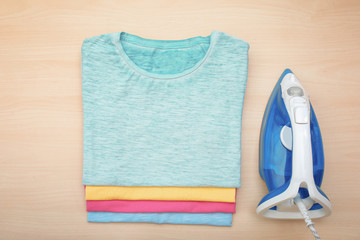 Folded clean clothes and iron on wooden background, top view