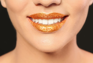 Fototapeta premium Beautiful young model with golden lips makeup on black background