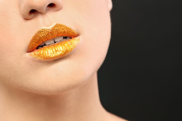 Beautiful young model with golden lips makeup on black background