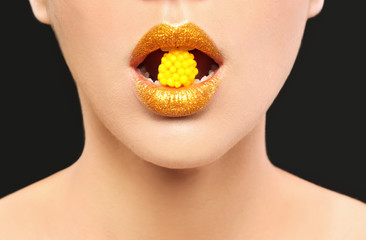 Beautiful young model with creative makeup holding candy in lips on black background