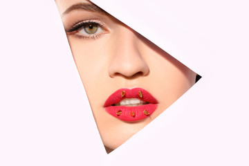 View of beautiful young woman with creative lips makeup through cutout in color paper