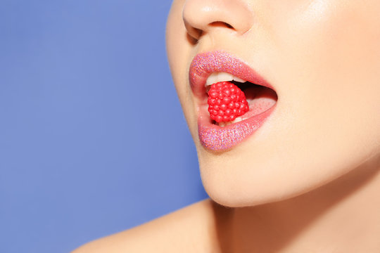 Beautiful young model with creative makeup holding candy in lips on color background