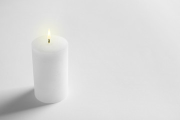 Pillar wax candle burning on white background