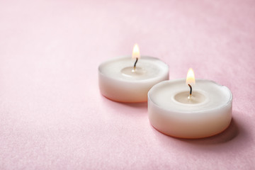 Small wax candles burning on color background