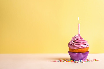 Delicious birthday cupcake with candle on color background