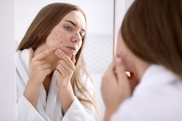 Obraz na płótnie Canvas Young woman with acne problem near mirror in bathroom