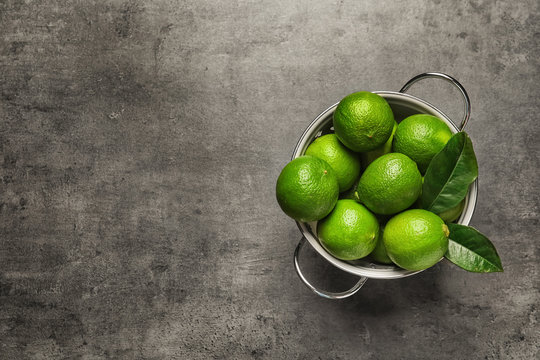 Colander with fresh ripe limes on gray background, top view