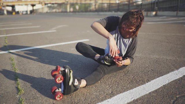 attractive hipster female  fix roller skates on the street at sunset